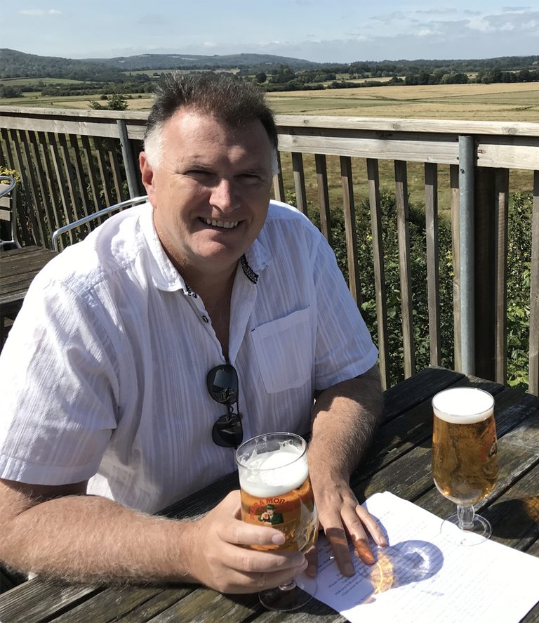 Andy Shaw smiling with a drink on a sunny terrace